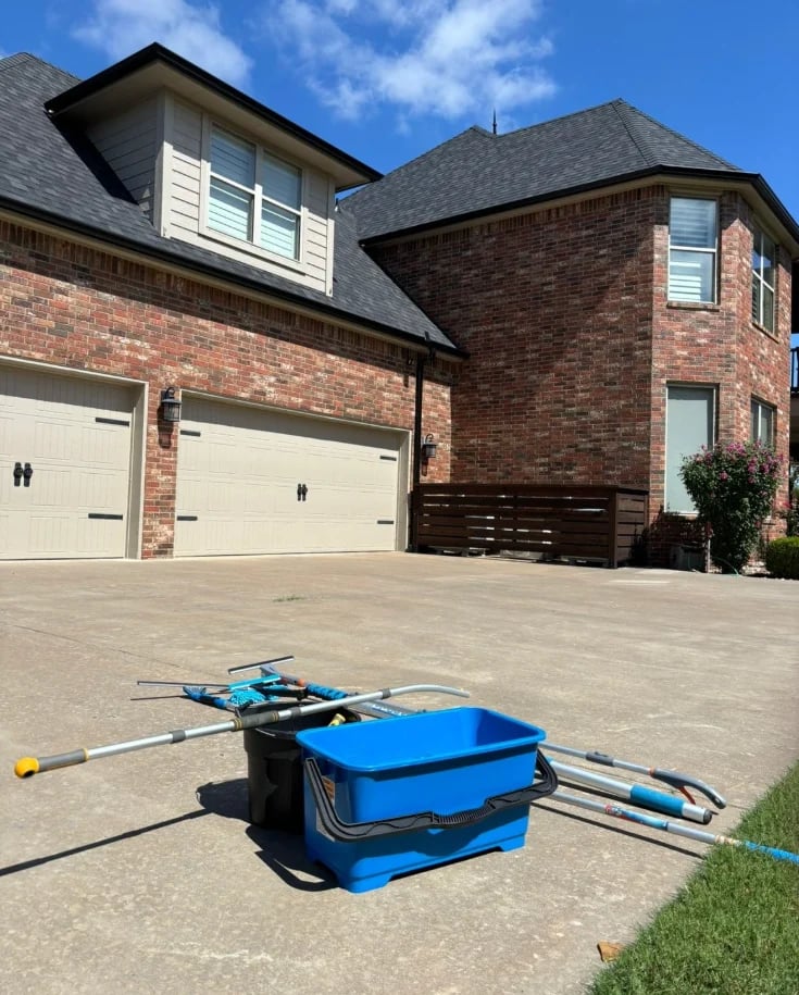 Blue power washing equipment on driveway in front of brick two-story house with white garage doors