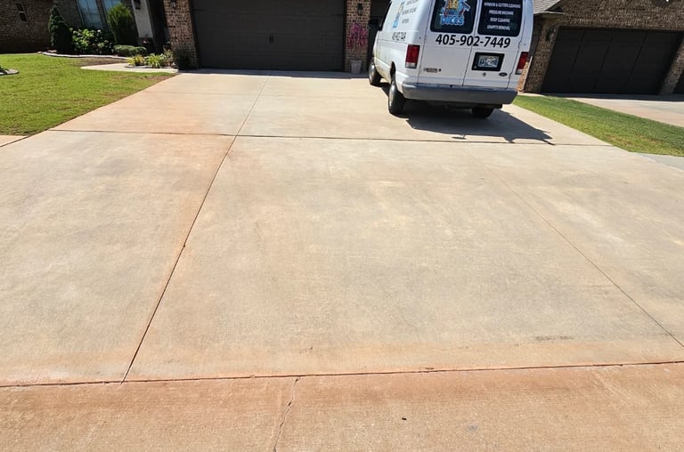 Wide residential driveway with concrete sections, white service van parked on it, black garages and green lawn visible in background